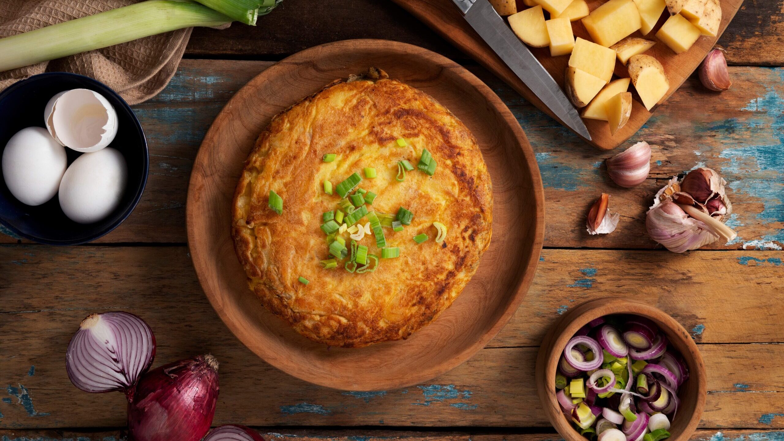 Ein leckerer argentinischer kartoffelkuchen auf einem rustikal wirkenden Untergrund, rundum Zutaten wie Zwiebel und Knoblauch