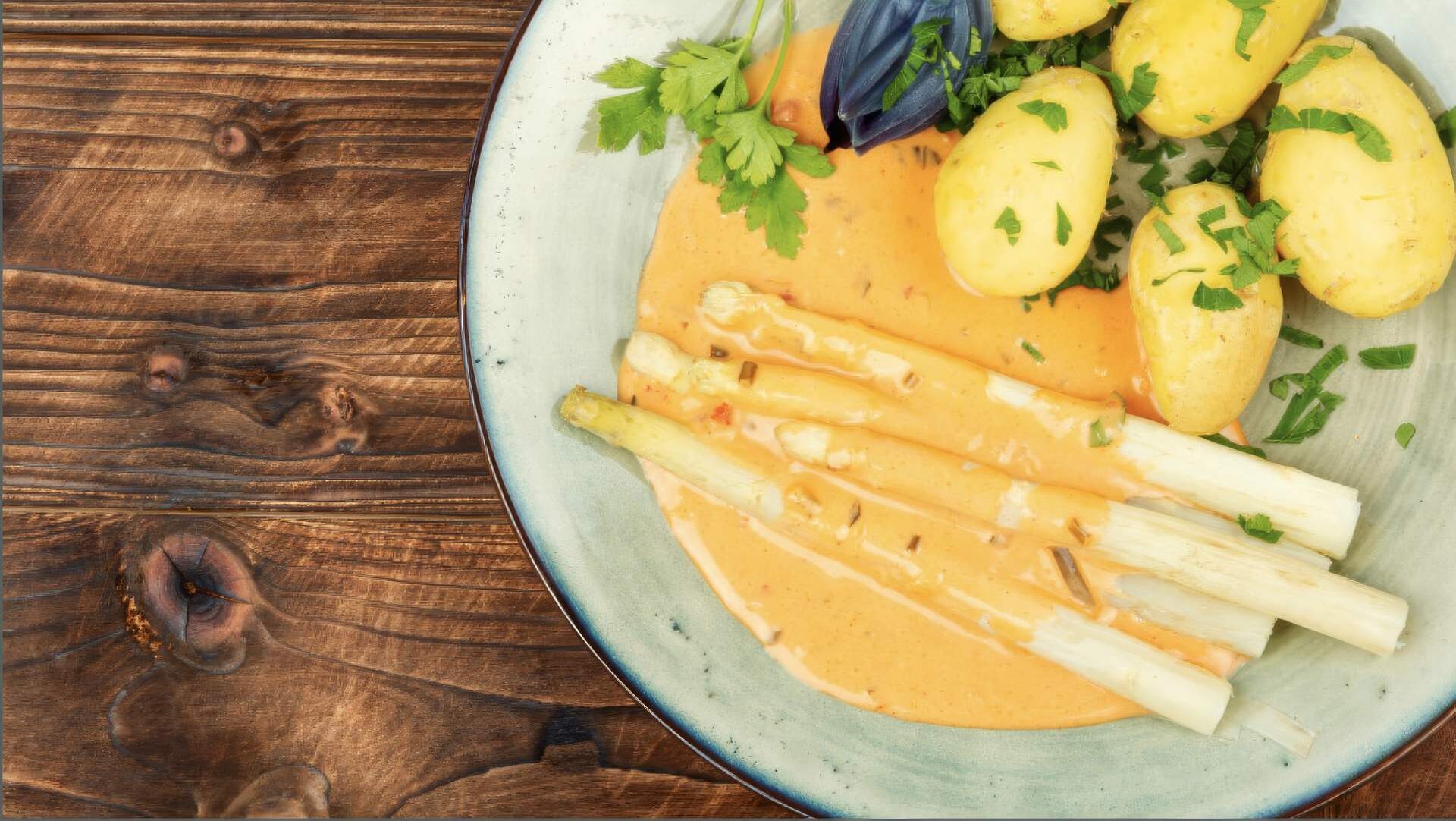 Ein Teller mit Spargel, Sauce Hollandaise und Kartoffeln auf eine braunen Holztisch