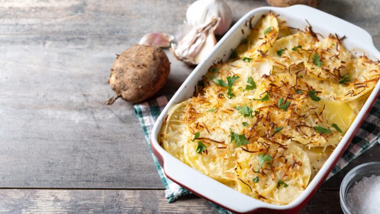 Eine lecker dnpfende Auflaufform mit Kartoffeln auf einem grauen Holztisch