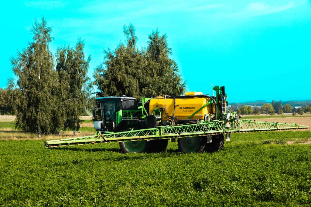 Gelber DAMMANN Profi-Class Pflanzenschutz-Traktor auf einem grünen Feld unter blauem Himmel"
