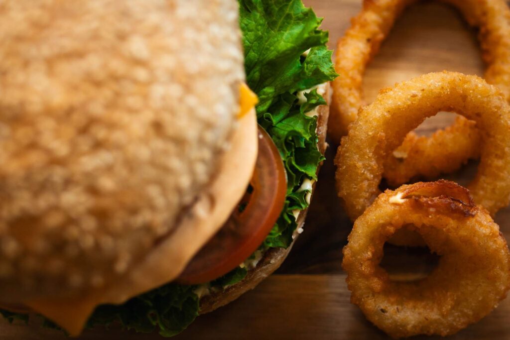 Extreme Nahaufnahme eines Burgers und der knusprigen, goldbraunen Zwiebelringe auf einem Holzbrett, die Struktur der Zutaten ist deutlich erkennbar.