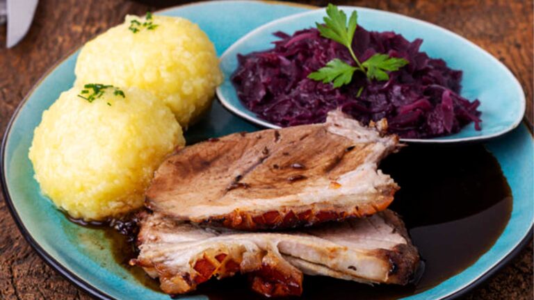 Teller mit traditionellen Thüringer Klößen und Schweinebraten mit knuspriger Kruste, Rotkohl und dunkler Soße, garniert mit Petersilie. Im Hintergrund ein Beilagensalat. Das Bild enthält die Textelemente "Let's Cook", "traditionell", "Thüringer Klöße", "Zubereitungszeit: 80 Min.", "Zutaten für 6 Personen", "saisonal" und "gleich abspeichern!"