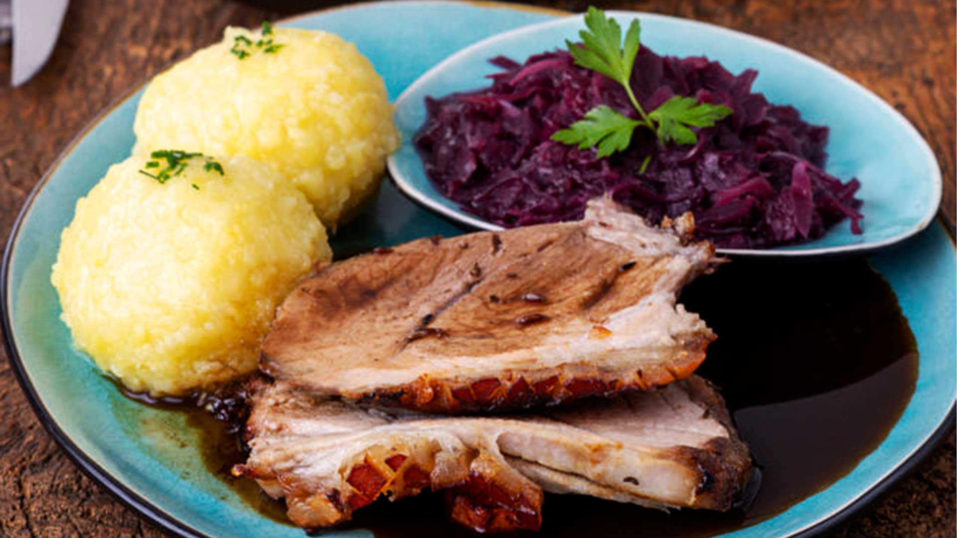 Teller mit traditionellen Thüringer Klößen und Schweinebraten mit knuspriger Kruste, Rotkohl und dunkler Soße, garniert mit Petersilie. Im Hintergrund ein Beilagensalat. Das Bild enthält die Textelemente "Let's Cook", "traditionell", "Thüringer Klöße", "Zubereitungszeit: 80 Min.", "Zutaten für 6 Personen", "saisonal" und "gleich abspeichern!"