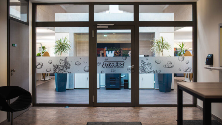 Moderner Eingangsbereich der Friweika mit Glastüren, Firmenlogo und dekorativem Kartoffel-Design auf der Sichtschutzfolie.