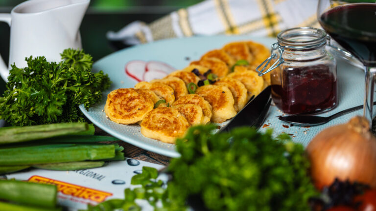 Goldbraun gebratene Wickelkloß-Scheiben auf einem Teller mit Preiselbeeren, Kräutern und Rotwein.