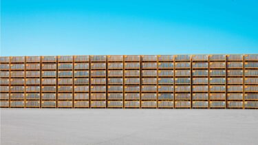 Effiziente Logistik und Lagerung bei Friweika: Fachgerecht gestapelte Großkisten für Kartoffeln auf einem Betriebsgelände vor blauem Himmel.