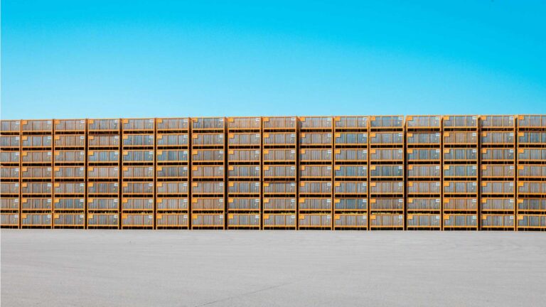 Effiziente Logistik und Lagerung bei Friweika: Fachgerecht gestapelte Großkisten für Kartoffeln auf einem Betriebsgelände vor blauem Himmel.