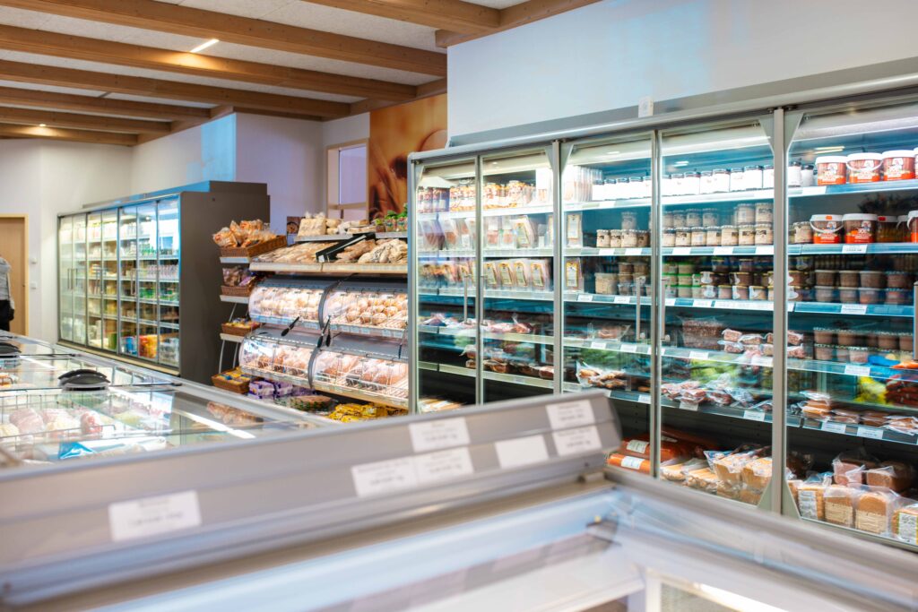 Umfangreiches Sortiment im Friweika Werksverkauf: Übersichtliche Kühlregale mit Fleisch- und Wurstwaren sowie Backwarenstation in moderner Ladenatmosphäre.