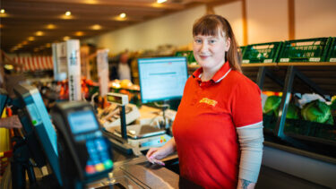 Freundlicher Kundenservice bei Friweika: Lächelnde Mitarbeiterin in roter Arbeitskleidung an einer modern ausgestatteten Kasse im Werksverkauf.