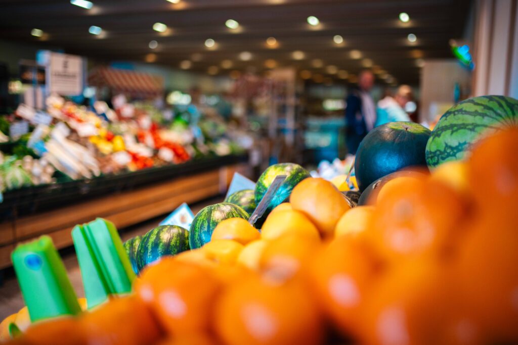 Frisches Obstangebot im Friweika Werksverkauf: Fokus auf Melonen und Zitrusfrüchte in der Auslage, mit Blick in den gut sortierten Verkaufsraum.