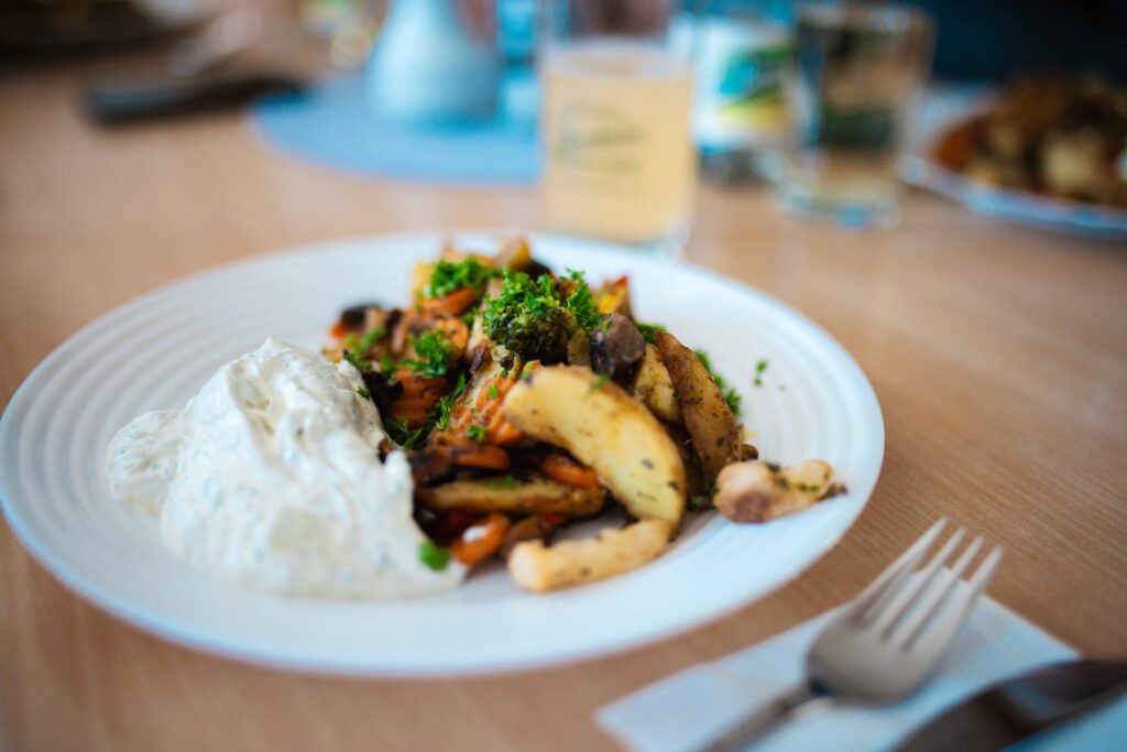 Frisches Gericht bei Friweika: Goldbraun geröstete Kartoffelspalten mit buntem Pfannengemüse (Brokkoli, Karotten) und einem cremigen Kräuterquark-Dip, garniert mit Petersilie.