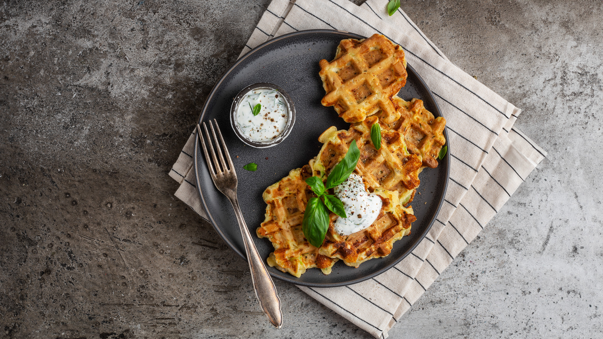 Herzhafte Kartoffel-Waffeln mit Kräuterquark und frischem Basilikum auf einem dunklen Teller.