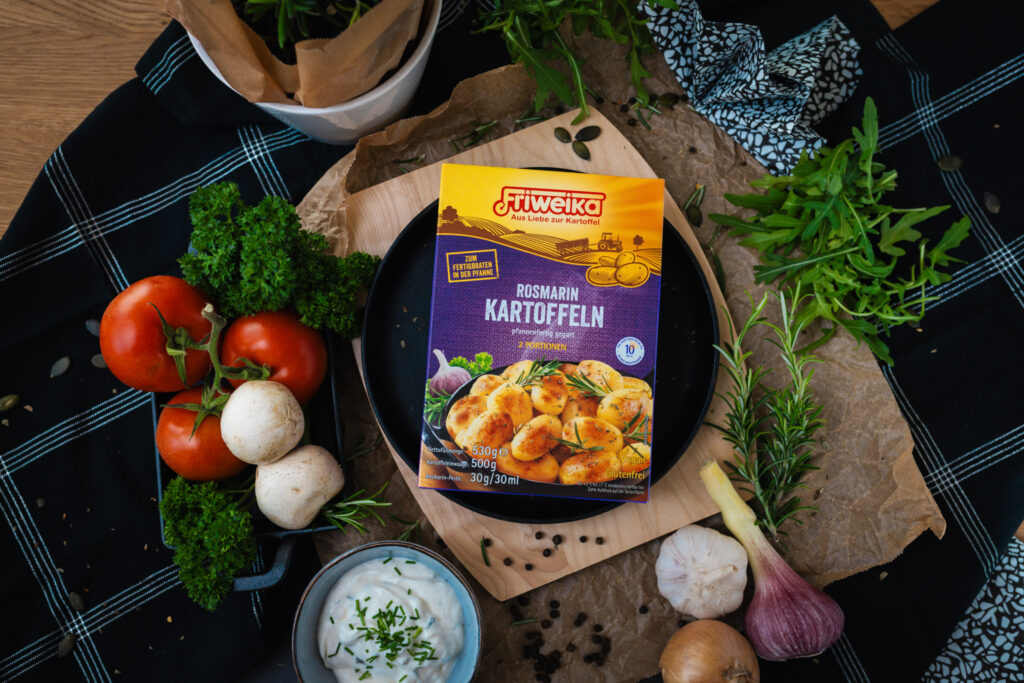 Friweika Rosmarinkartoffeln Produktpackung in einer Draufsicht mit frischen Tomaten, Pilzen, Knoblauch und Dip arrangiert