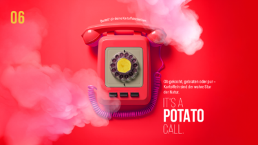Rotes Retro-Telefon mit einer Kartoffelscheibe im Wähldrehrad auf rotem Hintergrund mit rosa Rauch und dem Text „IT'S A POTATO CALL.“