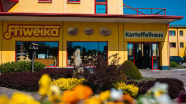 Gelbes Firmengebäude der Friweika eG mit dem Schriftzug „Kartoffelhaus“ und bepflanztem Vorgarten.