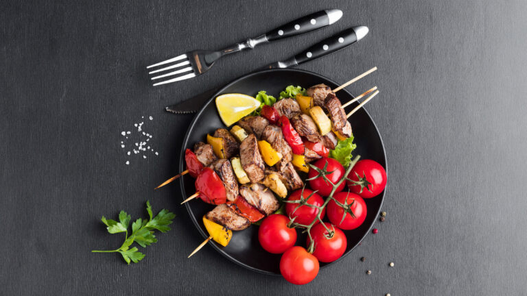 Grillspieße mit Fleisch und buntem Gemüse auf einem schwarzen Teller mit Kirschtomaten