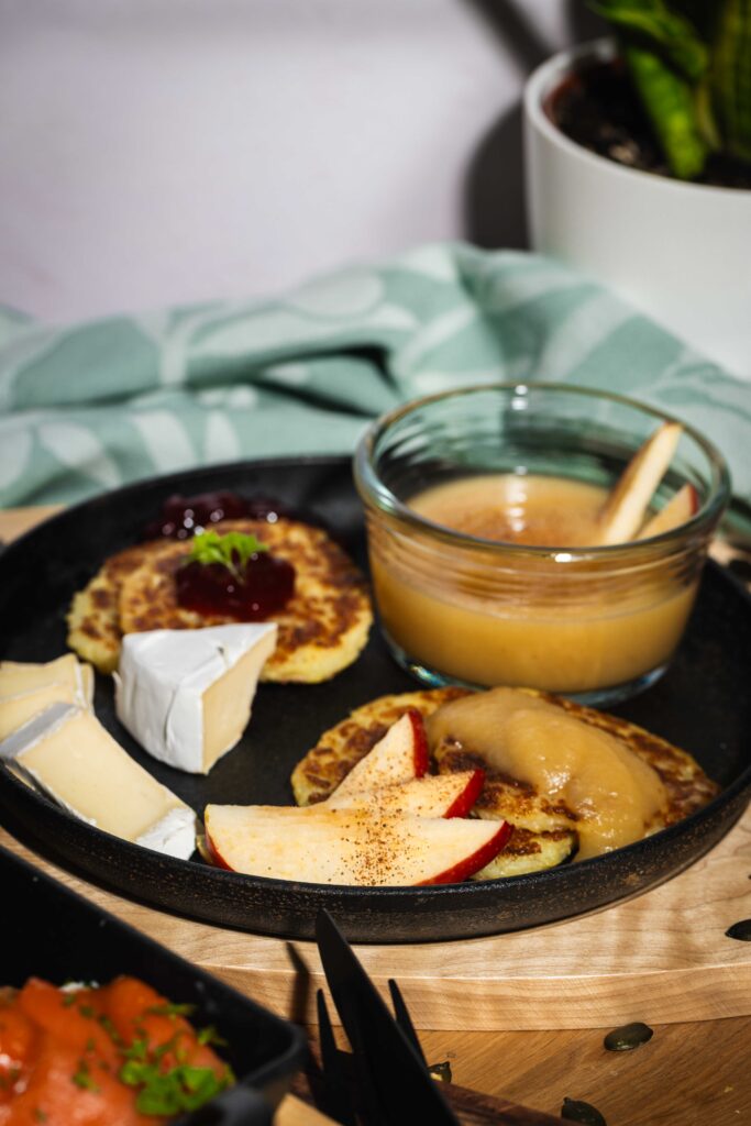 Teller mit goldenen Kartoffelpuffern, frischen Apfelscheiben, Käse und Apfelmus