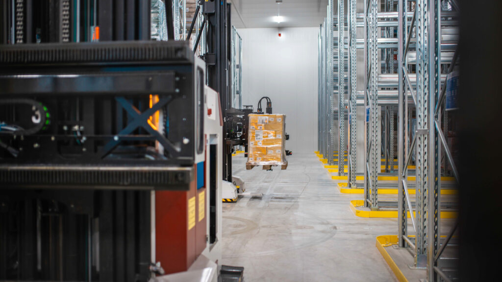 Fahrerloses Transportsystem (FTS) hebt verpackte Warenpalette in einem automatisierten Hochregallager.