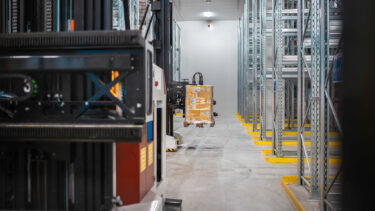 Fahrerloses Transportsystem (FTS) hebt verpackte Warenpalette in einem automatisierten Hochregallager.