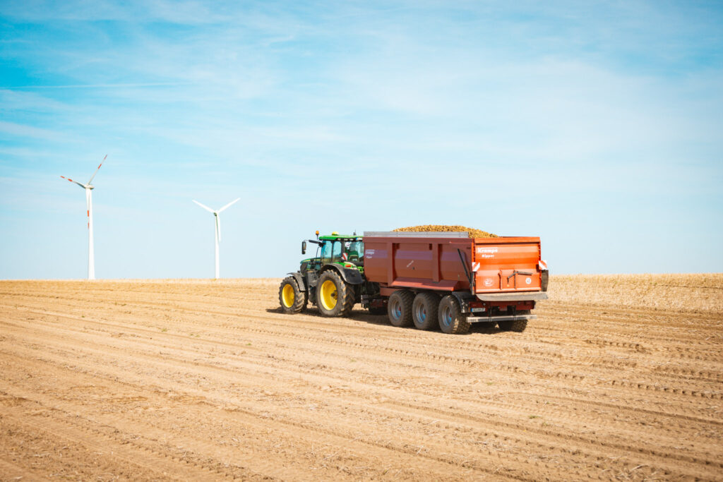 Grüner John Deere Traktor zieht beladenen Krampe-Anhänger mit Kartoffeln über ein abgeerntetes Feld