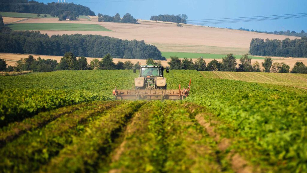 Traktor bei der Ernte auf einem grünen Feld vor hügeliger Kulisse.