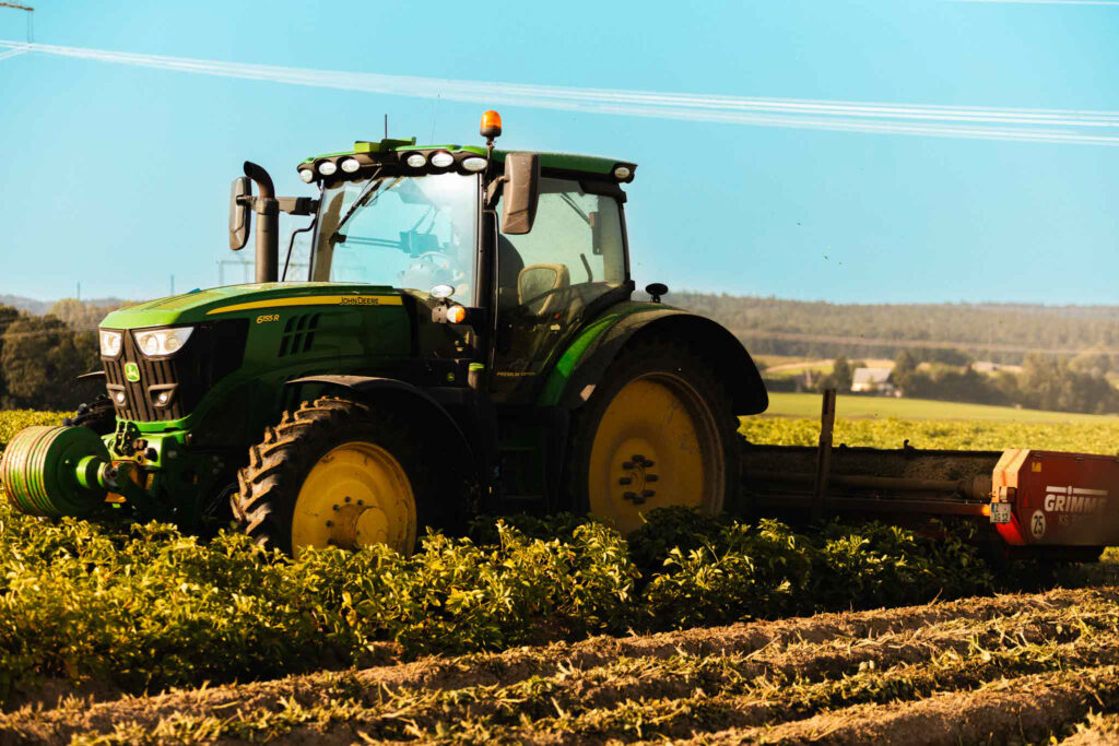 Grüner John Deere Traktor mit Grimme-Anbaugerät bei der Feldarbeit