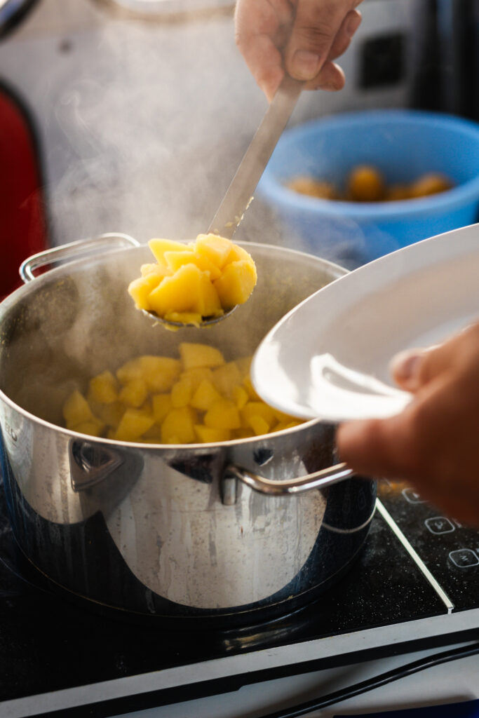 Dampfende gekochte Kartoffeln werden mit einem Schaumlöffel aus dem Topf gehoben