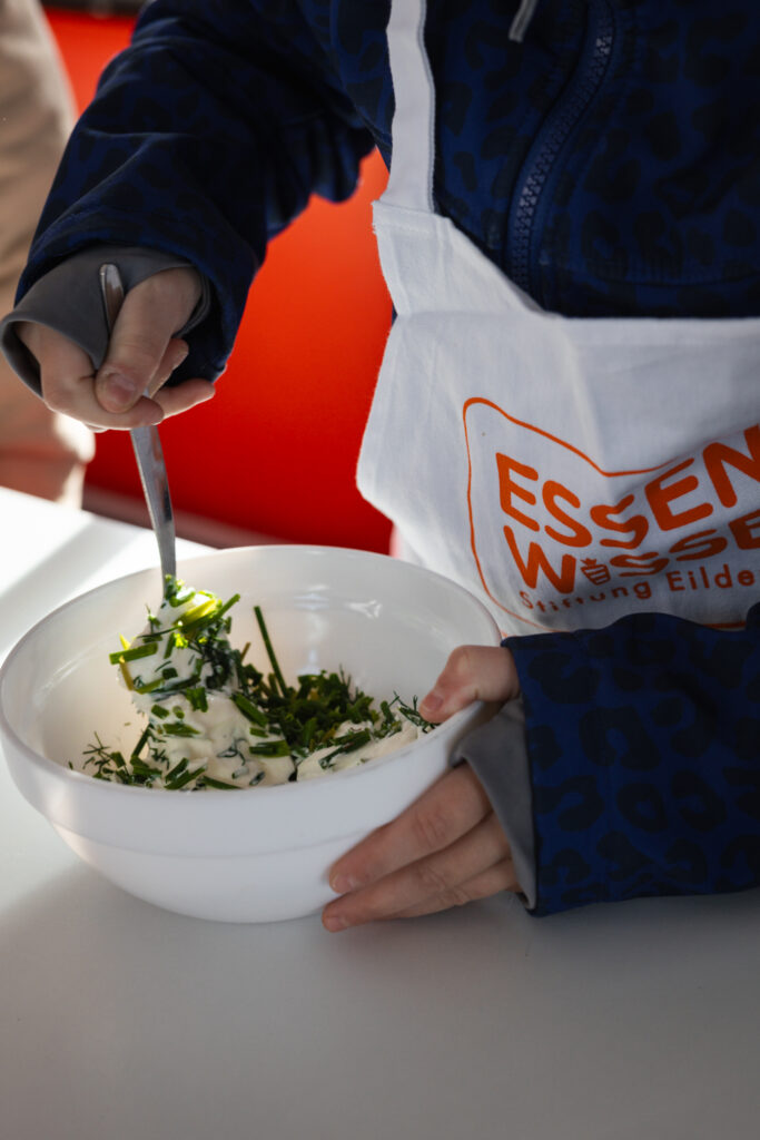 Kind verrührt Kräuterquark in einer Schüssel mit einer Essen-Wissen-Schürze