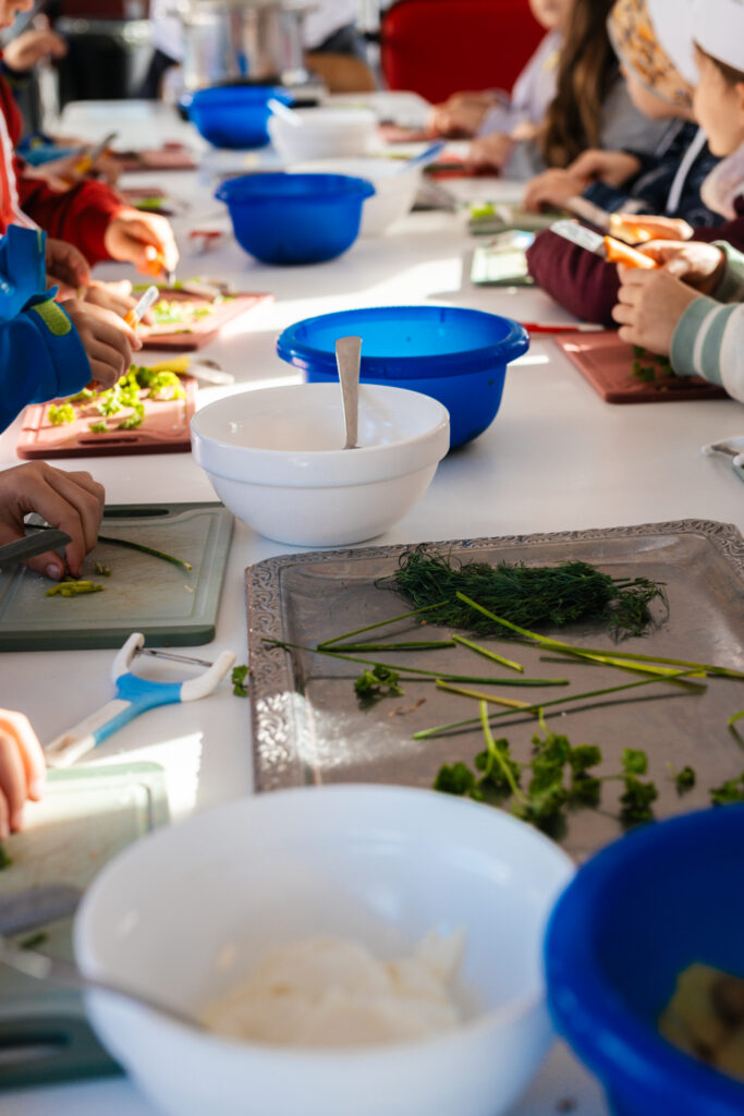 Kinder schneiden Kräuter an einer langen Kochecke im Kochbus