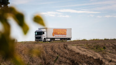 Weißer Friweika LKW mit der Aufschrift Aus Liebe zur Kartoffel fährt auf einer Landstraße am Feld entlang