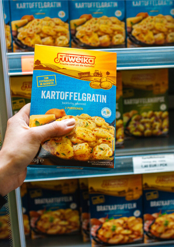 Hand nimmt eine Packung Friweika Kartoffelgratin aus dem Supermarktregal